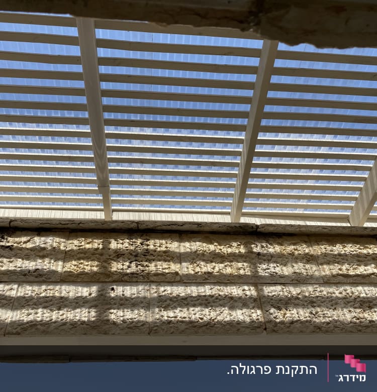 פרגולה מעץ עם קורות לבנות בשמש